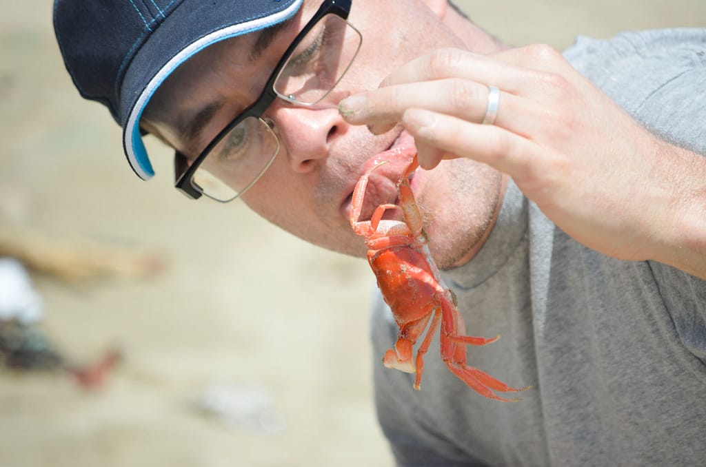 A man sticks out his tongue at a crab as he lifts it in the air