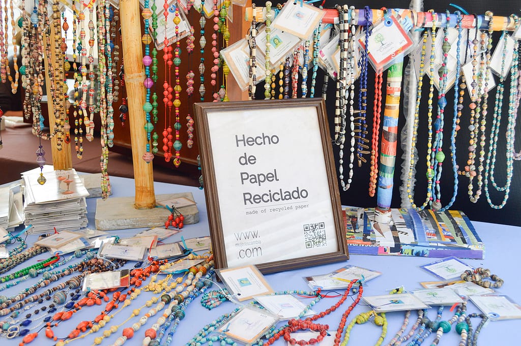 A table with Mujeres: Cambia jewelry with a sign that reads, "hecho de papel reciclado"