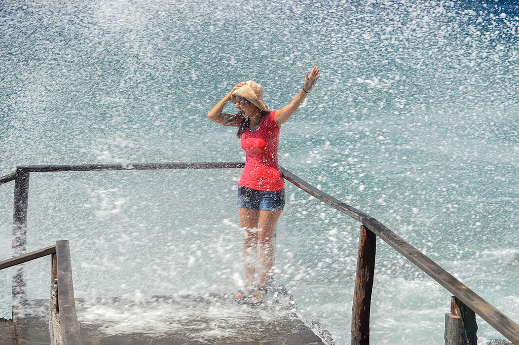 A woman  wearing a red shirt is splashed by a big wave in the Galapagos