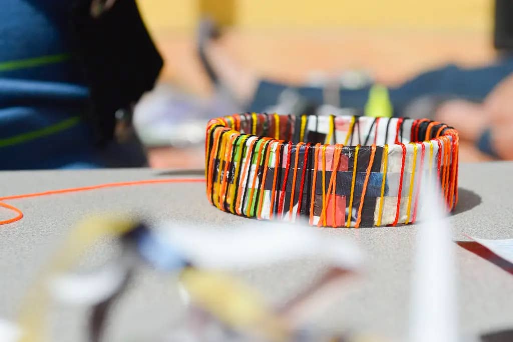 A close up image of a bracelet made of magazine paper and embroidery floss