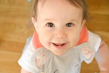 A one-year-old child wearing a bib looks up at the camera