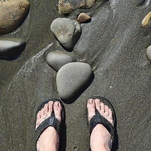 Feet wearing flip flops on top of black sand