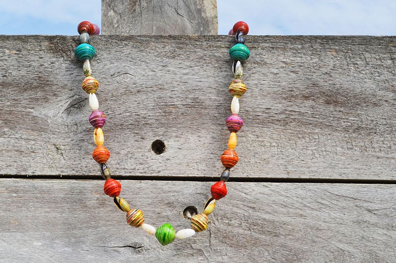 A paper bead necklace by Mujeres: Cambia hangs on a wooden fence