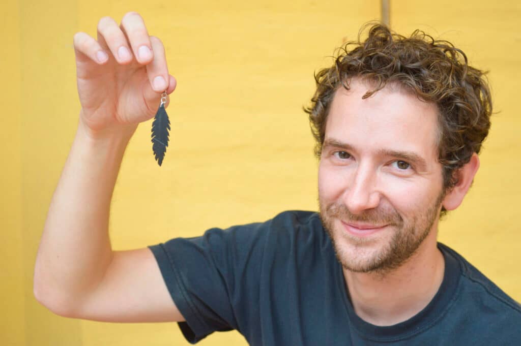Paul Wilson holds an earring made from recycled rubber in the shape of a feather